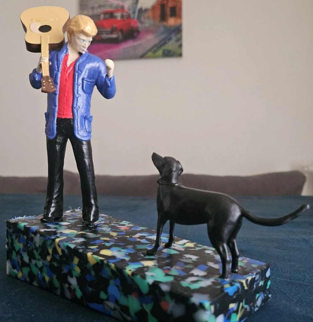 Figurine peinte de Johnny Hallyday avec sa guitare et un chien noir, sur socle terrazzo